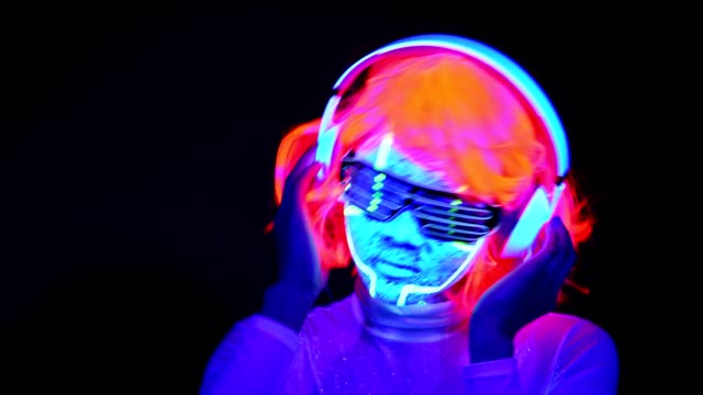 Woman-with-UV-cyborg-face-paint,-wig,-glowing-glasses,-clothing-dancing-and-listening-to-music-with-headphones.-Asian-woman.-.