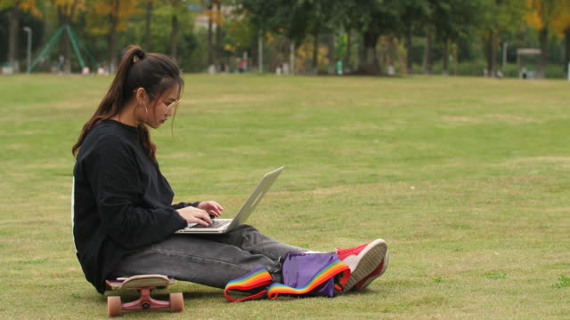 Asiatische-College-Mädchen-sitzen-auf-Skateboard-mit-Laptop-auf-dem-campus