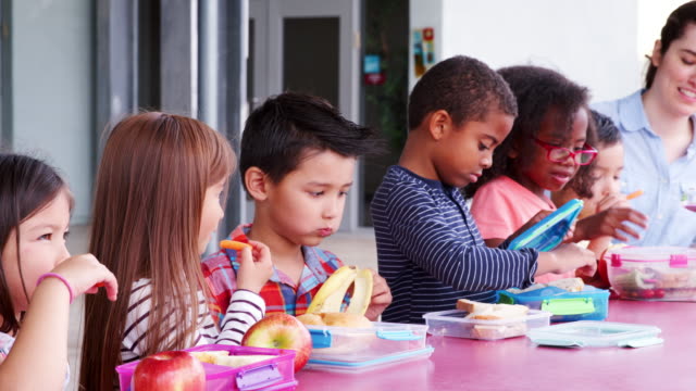 Escuela-primaria-niños-comiendo-en-la-mesa-con-comidas