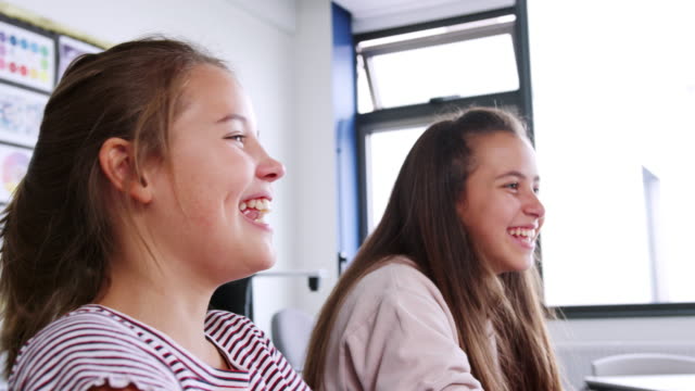 Zwei-weibliche-Schülerinnen-und-Schüler-lachen,-als-sie-im-Klassenzimmer-sitzen