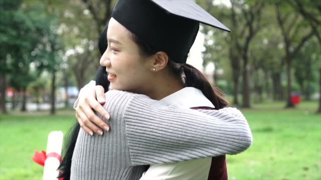 Young-Asian-female-graduate-hugging-her-friend-at-graduation-ceremony-in-slow-motion.-International-diversity-background