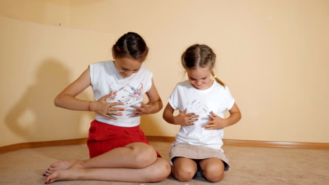 Kleine-Schwestern-sitzen-auf-Boden-und-malen-ein-T-shirt-mit-ihren-Händen