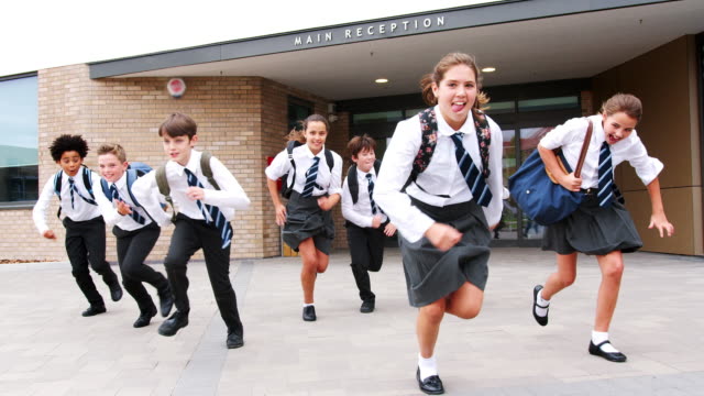 Gruppe-von-Schülerinnen-und-Schüler-tragen-gleichmäßigen-Lauf-aus-Schulgebäude-in-Richtung-Kamera-am-Ende-der-Klasse