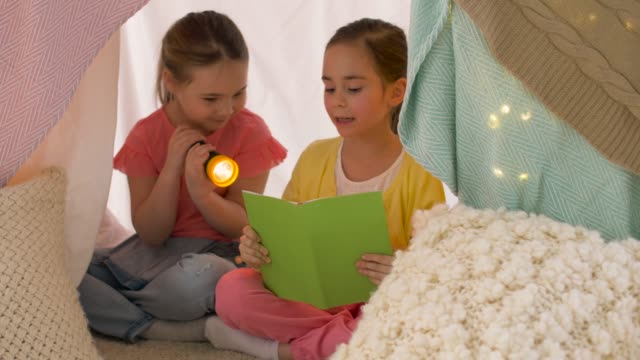 happy-girls-reading-book-in-kids-tent-at-home