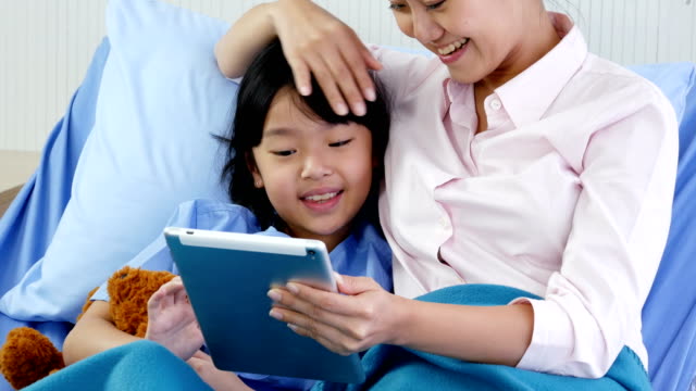 Kleine-Mädchen-und-ihre-Mutter-mit-Tablette-zusammen-im-Krankenhaus.-Menschen-mit-Technik,-Familie,-Gesundheits--und-medizinische-Konzept.