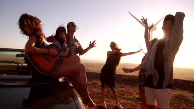 Hipster-friends-enjoying-road-trip-with-a-guitar-during-sunset