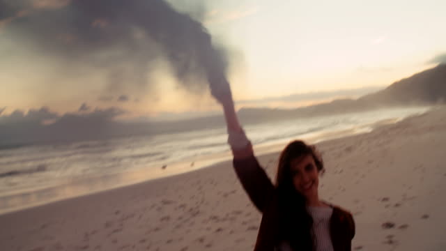 Attractive-Boho-Hipster-Girl-walking-on-Beach-with-smoke-flare