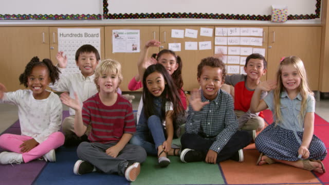 Niños-de-escuela-primaria-clase-Siéntese-saludar-con-la-mano-a-la-cámara