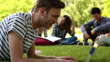 Student-using-laptop-and-classmates-speaking-behind-him