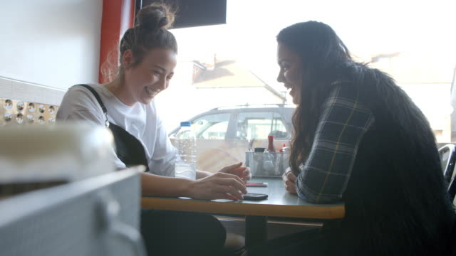 Zwei-Studentinnen-im-Cafe-überprüfen-Sie-Nachrichten-auf-dem-Handy
