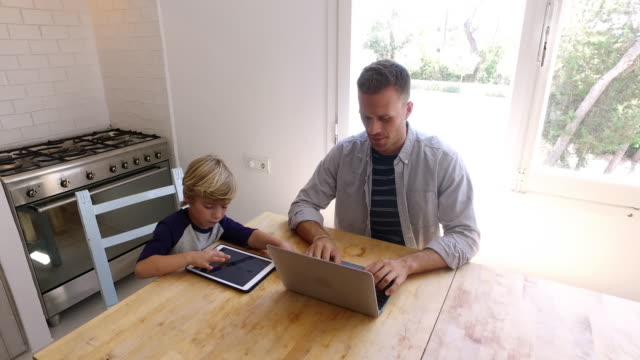 Padre-e-hijo-usando-computadoras-en-la-mesa-de-la-cocina