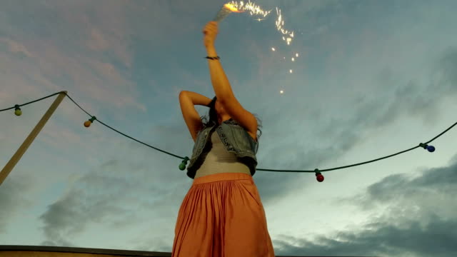 Under-view-of-brunette-woman-jumping-with-firework-candle-on-the-rooftop-terrace