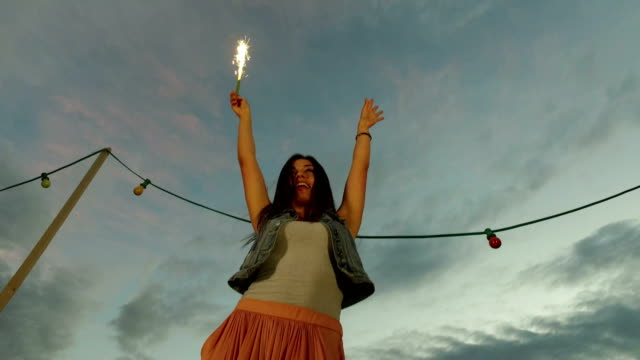 Low-angle-view-of-happy-woman-jumping-with-firework-candle
