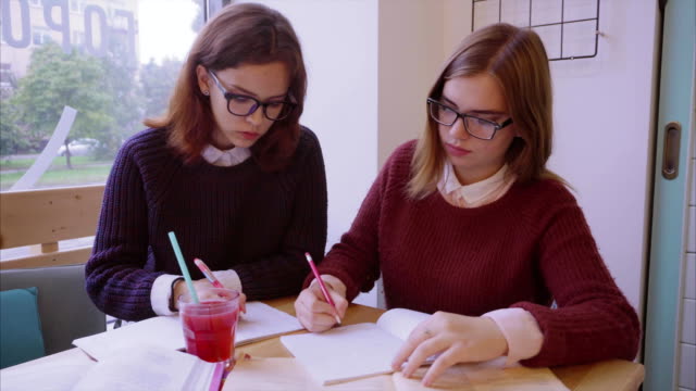 Female-college-students-studies-in-the-cafe-two-girls-friends-learning-together