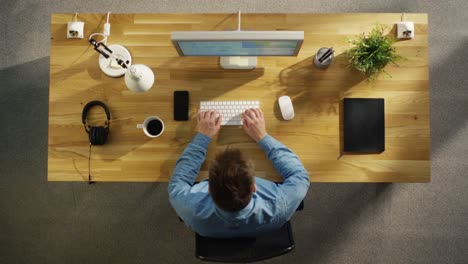 Top-Ansicht-eines-Software-Ingenieurs,-der-an-einem-Desktop-Computer-sitzt,-der-an-seinem-Tisch-sitzt.-Tisch-ist-Neat,-Smartphone,-Plant,-Coffee-Cup,-Kopfhörer-liegen-darauf.