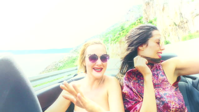 Zwei-glückliche-Mädchen-feiern-während-der-Fahrt-im-Cabriolet,-benotet-mit-Gelbfilter