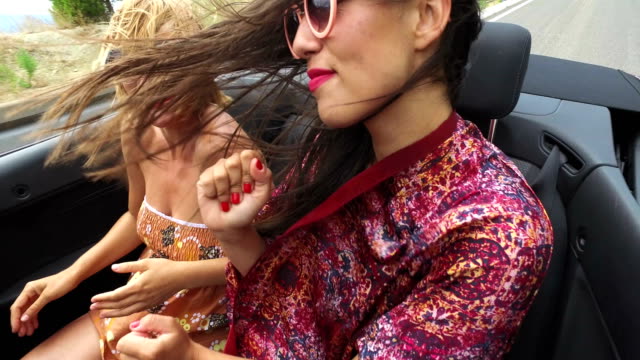 Zwei-glückliche-Mädchen-feiern-während-der-Fahrt-im-cabriolet