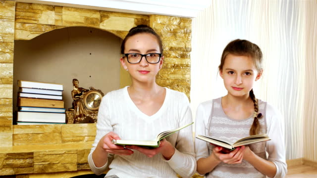 sisters-reading-textbooks-near-fireplace-at-home,-girls-smiling-and-hugging,-wearing-glasses
