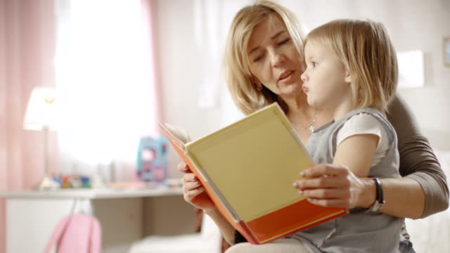 Cute-Little-Girl-Sits-on-Her-Grandmother's-Lap-and-They-Read-Children's-Book.-Slow-Motion.