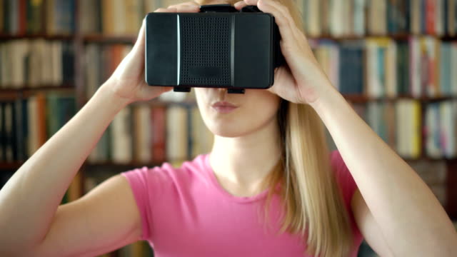 Glückliche-Schüler-stehen-in-der-Bibliothek-mit-virtual-Reality-Brille.-Bücherregale-Bücherregal-im-Hintergrund