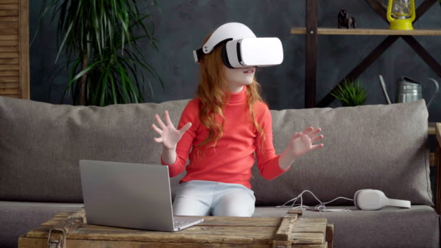 Little-girl-is-sitting-on-the-sofa-in-the-room-in-vr-headset-and-dong-something-with-the-hands