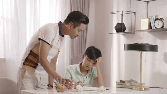Asiatischen-Vater-zu-Fuß-in-Lesesaal-im-Gespräch-mit-Sohn-bei-den-Hausaufgaben-frustriert