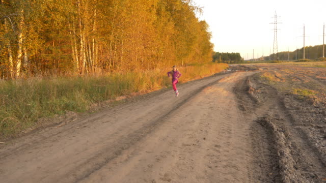 Chica-corriendo-y-girando-en-carretera-tarde-otoño.-Jovencita-al-aire-libre-panorámica-de-longitud-total.
