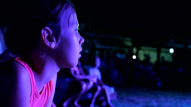Sommer,-Nacht,-in-den-Strahlen-der-Laibungen,-ein-Mädchen-von-sieben-Jahre-alt,-gerade-die-Nachtkonzert-in-ein-Open-Air-Theater-im-Urlaub.-viele-Kinder-sind-im-Hintergrund