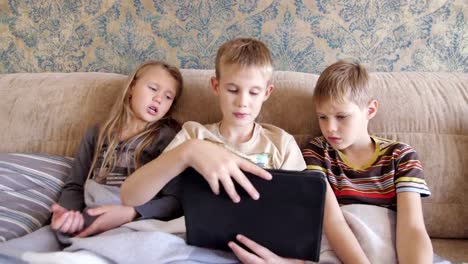 Kinder-spielen-auf-dem-Tablet-im-Hause-auf-der-Couch-sitzen