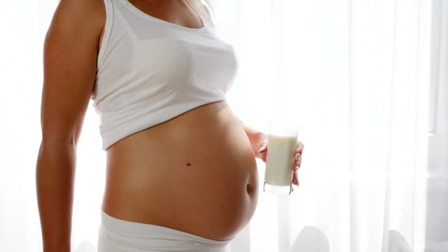 mujer-embarazada-muestra-simvol-de-aprobación-y-tiene-leche-de-cristal-sobre-fondo-de-gran-barriga,-productos-lácteos