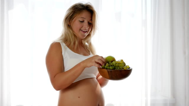 Ernährung-während-der-Schwangerschaft-isst-Frau-mit-einem-großen-Bauch-Trauben-aus-einer-Holzplatte