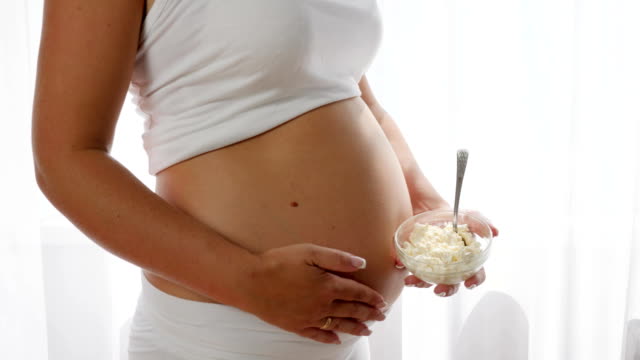 Close-up-Platte-mit-Quark-in-der-Hand-einer-schwangeren-Frau-in-der-Nähe-einen-großen-nackten-Bauch
