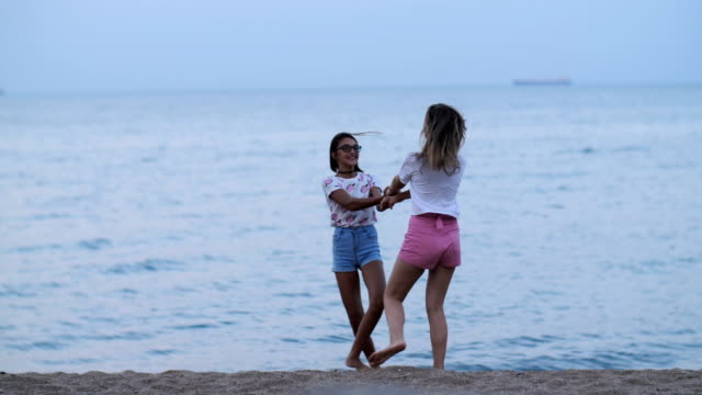 zwei-glückliche-Mädchen-Wirbeln-am-Strand-in-der-Nähe-von-das-Meer-am-Abend