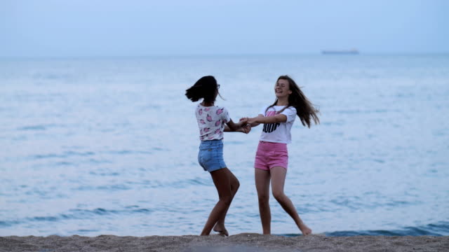 zwei-glückliche-Mädchen-Wirbeln-am-Strand-in-der-Nähe-von-das-Meer-am-Abend