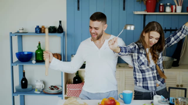 Young-joyful-couple-have-fun-dancing-and-singing-while-set-the-table-for-breakfast-in-the-kitchen-at-home