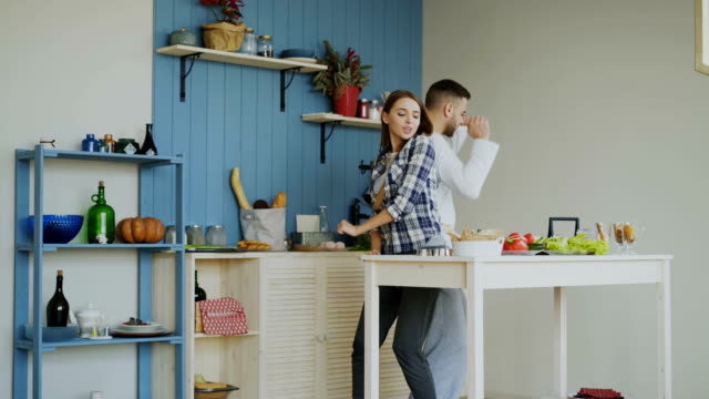 Attraktives-junges-Paar-fröhlich-tanzen-beim-Kochen-in-der-Küche-zu-Hause