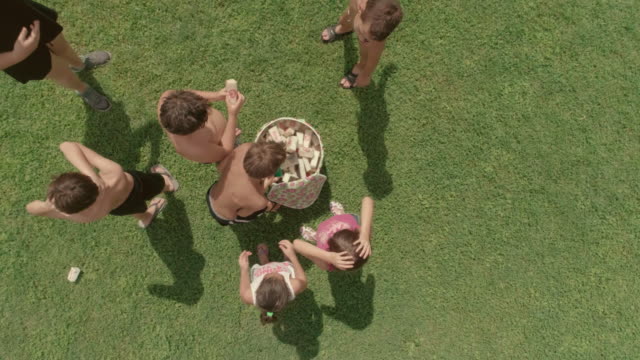 Top-view-kids-in-summer-camp-playing-in-green-grass-field-putting-sponges-in-bin-slow-motion-aerial-vertical
