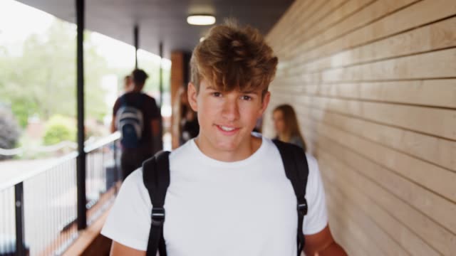 Portrait-Of-Male-Student-Walking-Into-Focus-Outside-Building