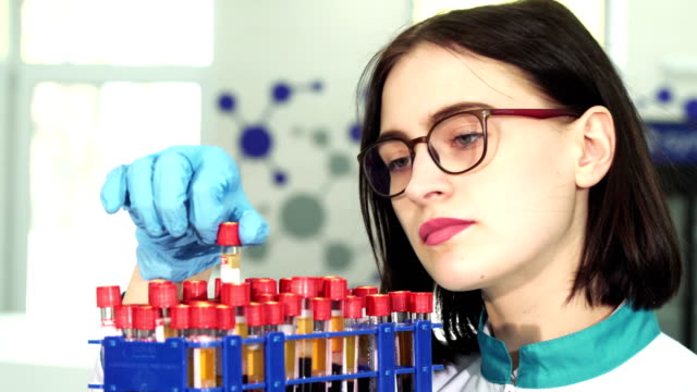 Cerca-de-un-joven-investigador-femenino-examen-de-tubos-de-ensayo-con-muestras-de-sangre