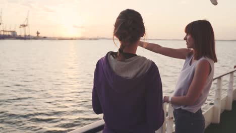 zwei-Freundinnen-tanzen-auf-dem-Deck-des-Schiffes-bei-Sonnenuntergang