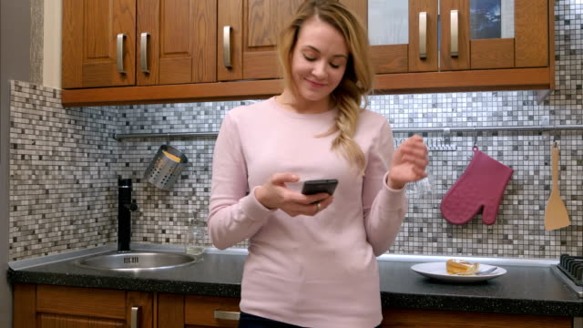 Glückliche-junge-Frau-tanzen-in-Küche-anhören-von-Musik-auf-Smartphone-zu-Hause