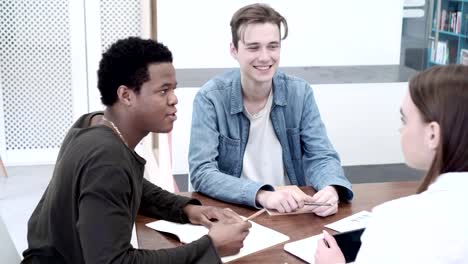 Team-of-three-diverse-college-students-making-a-project-together.-Medium-shot-of-fellow-students-sitting-at-desk-and-working-in-group