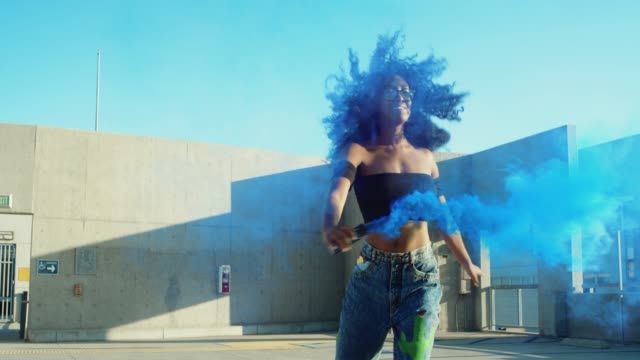 Young-woman-dancing-outside-with-smoke-grenade-at-sunset-on-rooftop-parking-garage