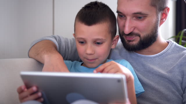 Delighted-father-hugging-son-while-using-tablet-on-sofa