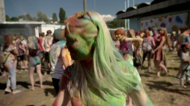 Young-happy-girl-in-colourful-powder-is-jumping-and-shaking-head-on-holi-festival-in-daytime-in-summer,-color-concept