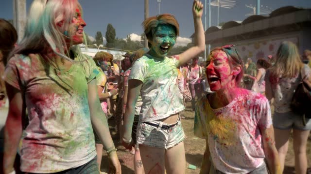 Tres-jóvenes-amigas-multiétnicas-están-saltando-y-bailando-con-polvo-colorido-en-el-festival-de-holi-en-horario-diurno-en-verano,-el-concepto-de-la-amistad,-el-concepto-del-color