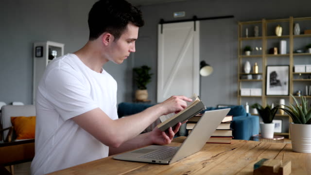 Junger-Mann-Lesebuch-und-arbeiten-am-Laptop