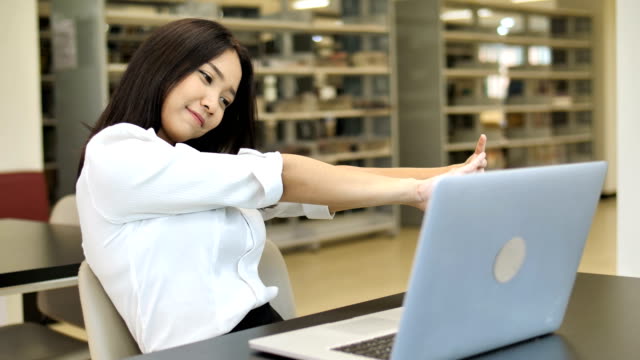 4K-Slow-Motion:-Porträt-von-einer-verschlafenen-schöne-asiatische-Studentin-mit-Laptop-in-der-Bibliothek