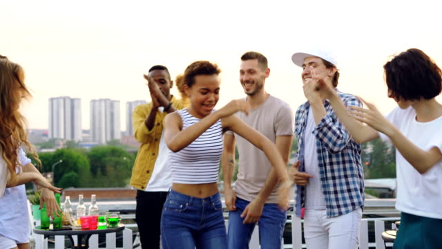 Pretty-mixed-race-girl-is-dancing-with-friends-and-laughing-enjoying-rooftop-party.-Entertainment,-partying-outdoors-and-modern-lifestyle-concept.