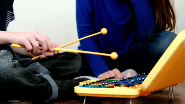 Playing-music-instrument.-Closeup-boy's-hand-playing-on-xylophone-and-his-mom-sitting-near-him.